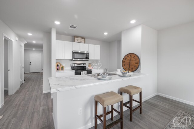 409 Garvin St, Eastland, TX 76448 - kitchen with stainless steel appliances, a sink, a kitchen bar, wood finished floors, and white cabinetry