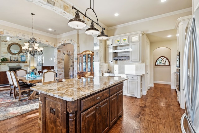 1100 Triple Crown Ct, Bartonville, TX 76226 - kitchen featuring arched walkways, light stone countertops, dark wood-style flooring, a stone fireplace, and crown molding