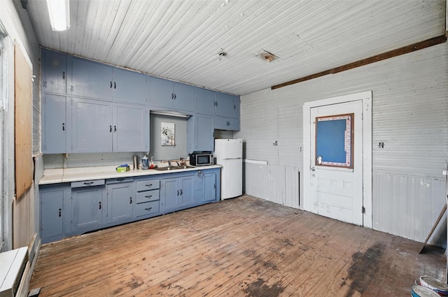 402 S Watson St, Alvarado, TX 76009 - kitchen with freestanding refrigerator, stainless steel microwave, blue cabinets, light countertops, and wood-type flooring