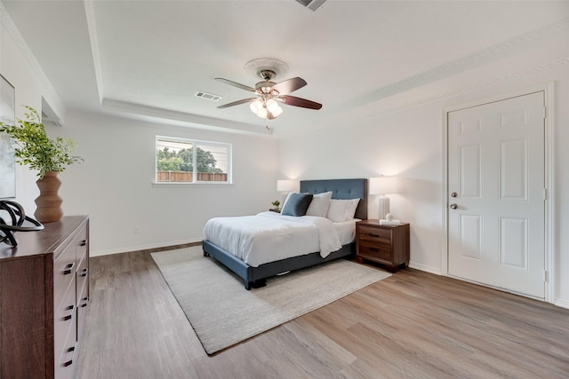 bedroom featuring light wood-style flooring, a raised ceiling, baseboards, and ceiling fan