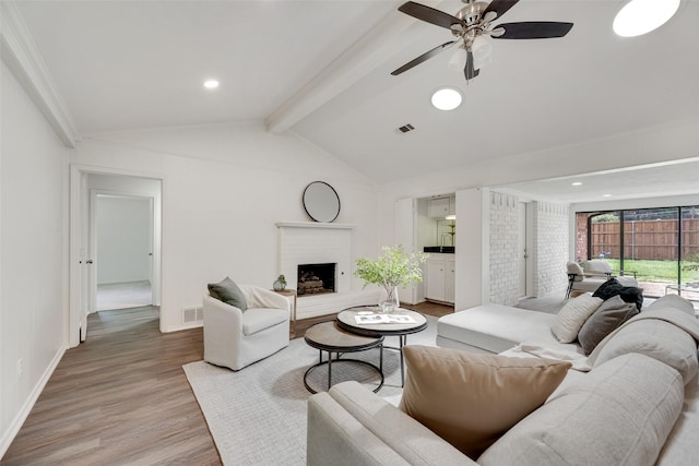 living room featuring light wood-style flooring, a ceiling fan, a brick fireplace, baseboards, and ornamental molding