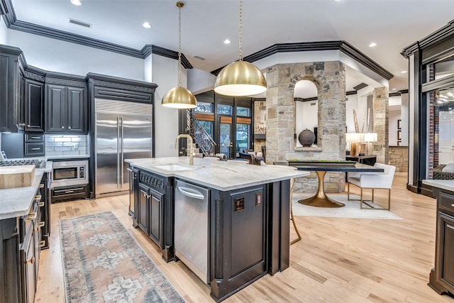 6616 Shoal Forest Ct, Plano, TX 75024 - kitchen featuring a sink, built in appliances, ornamental molding, light wood finished floors, and an island with sink