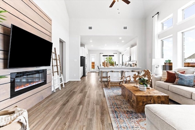 4342 Hudson St, Fate, TX 75087 - living area with light wood-style floors, ceiling fan, a towering ceiling, and a glass covered fireplace