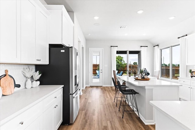 4342 Hudson St, Fate, TX 75087 - kitchen with a breakfast bar, white cabinets, wood finished floors, stainless steel fridge with ice dispenser, and light countertops