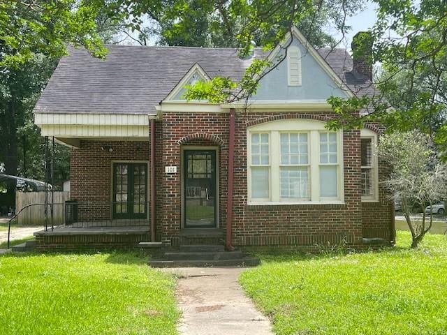 view of front of property with brick siding, a front yard, a chimney, and french doors