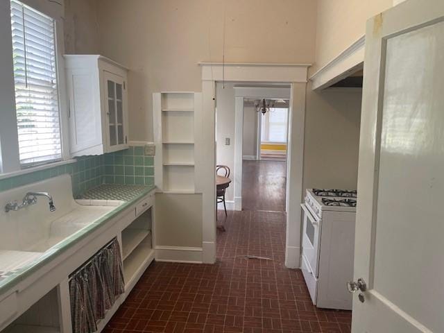 kitchen with white range with gas cooktop, white cabinetry, light countertops, baseboards, and glass insert cabinets