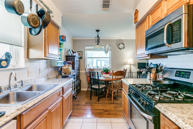 6900 Yorkston St, Watauga, TX 76148 - kitchen with appliances with stainless steel finishes, a sink, ornamental molding, brown cabinets, and pendant lighting