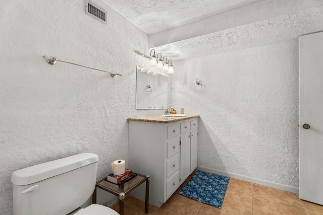 bathroom with a textured wall, toilet, vanity, baseboards, and tile patterned floors