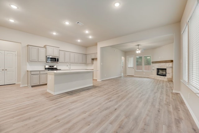 1301 Hickory Ct, Weatherford, TX 76086 - kitchen with stainless steel appliances, light wood-style flooring, ceiling fan, a fireplace, and light countertops