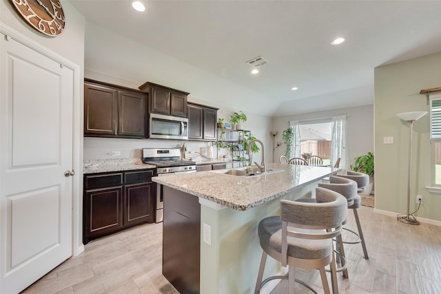 6128 Blacksmith Ave, Fort Worth, TX 76179 - kitchen with stainless steel appliances, a center island with sink, dark brown cabinets, recessed lighting, and a kitchen bar