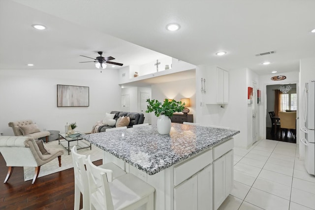 kitchen with light stone countertops, a ceiling fan, white cabinets, a center island, and open floor plan