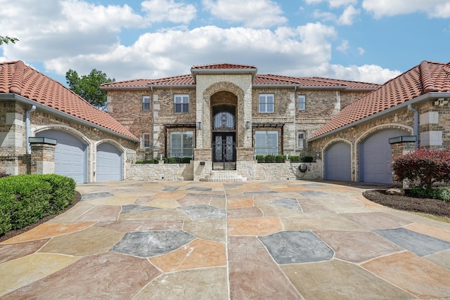 mediterranean / spanish house featuring a tiled roof, an attached garage, driveway, and stone siding