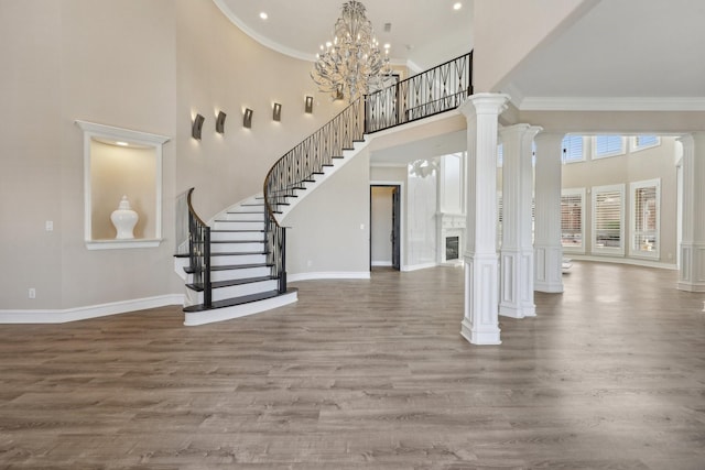 foyer with a high ceiling, wood finished floors, ornate columns, crown molding, and stairway
