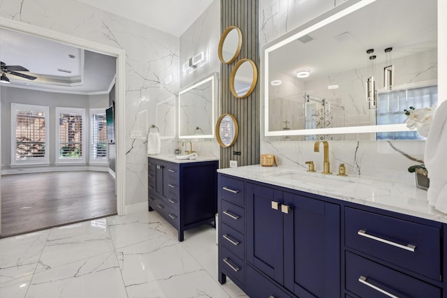 full bath featuring two vanities, marble finish floors, baseboards, a ceiling fan, and a raised ceiling