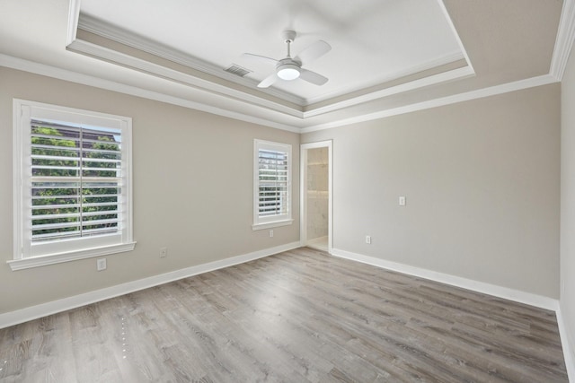 spare room featuring a raised ceiling, ornamental molding, a ceiling fan, wood finished floors, and baseboards
