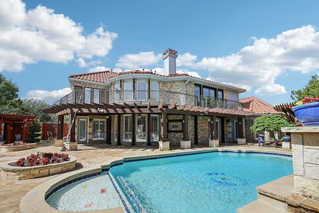 back of property with a tile roof, an outdoor pool, a patio, and stone siding