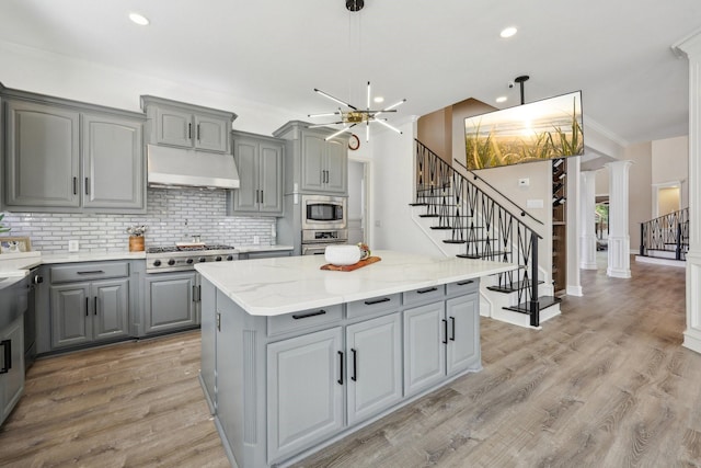 kitchen featuring gray cabinetry, under cabinet range hood, stainless steel appliances, a chandelier, and decorative backsplash