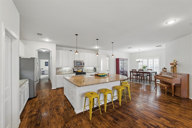 111 Blue Stem Ln, Aledo, TX 76008 - kitchen with stainless steel appliances, arched walkways, an island with sink, light stone countertops, and dark wood-type flooring