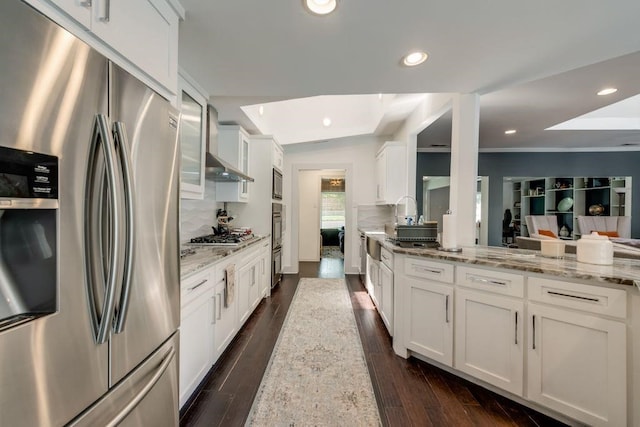 9178 Glen Springs Dr, Dallas, TX 75243 - kitchen featuring stainless steel appliances, wall chimney exhaust hood, white cabinets, tasteful backsplash, and light stone counters