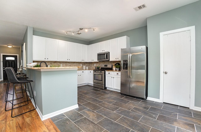 9305 Manassas Rdg, Mckinney, TX 75071 - kitchen featuring stainless steel appliances, a peninsula, a breakfast bar, backsplash, and white cabinets
