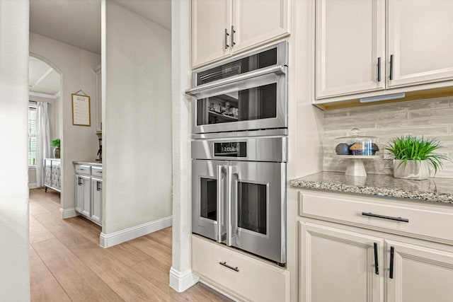 3204 Creek Meadow Dr, Anna, TX 75409 - kitchen featuring arched walkways, light wood-style floors, decorative backsplash, double oven, and light stone countertops