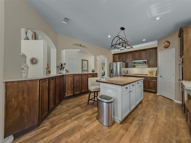 4305 Diplomacy Dr, Rowlett, TX 75089 - kitchen with appliances with stainless steel finishes, butcher block counters, arched walkways, wood finished floors, and a center island