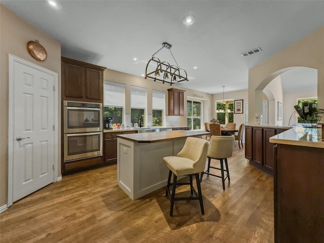 4305 Diplomacy Dr, Rowlett, TX 75089 - kitchen with stainless steel double oven, a kitchen island, a breakfast bar area, light countertops, and wood finished floors