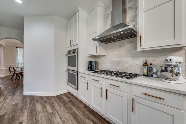 8016 Strecker Ln, Plano, TX 75025 - kitchen with wall chimney exhaust hood, arched walkways, appliances with stainless steel finishes, tasteful backsplash, and white cabinets