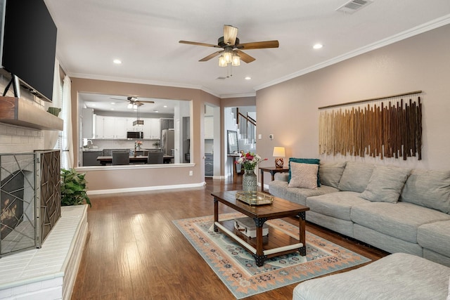 living area featuring ceiling fan, a brick fireplace, light wood-type flooring, ornamental molding, and recessed lighting