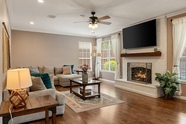 living room featuring baseboards, a ceiling fan, a brick fireplace, ornamental molding, and wood finished floors