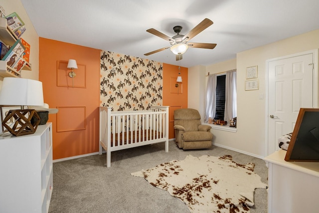 bedroom with carpet floors, a crib, baseboards, ceiling fan, and an accent wall