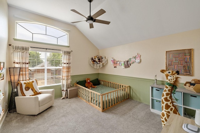 bedroom with lofted ceiling, a nursery area, wainscoting, carpet floors, and ceiling fan