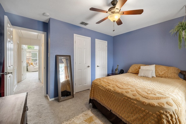 bedroom with attic access, light carpet, multiple closets, a ceiling fan, and baseboards