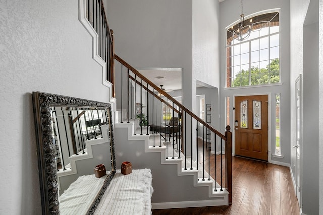 foyer entrance featuring a chandelier, dark wood-style floors, stairs, a high ceiling, and baseboards
