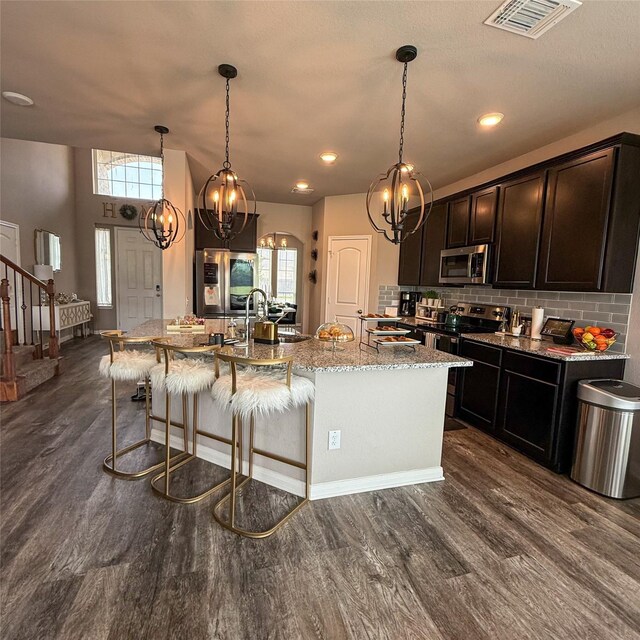 5202 Fallen Tree Dr, Temple, TX 76502 - kitchen featuring stainless steel appliances, a chandelier, dark wood-style floors, light stone countertops, and a kitchen island with sink