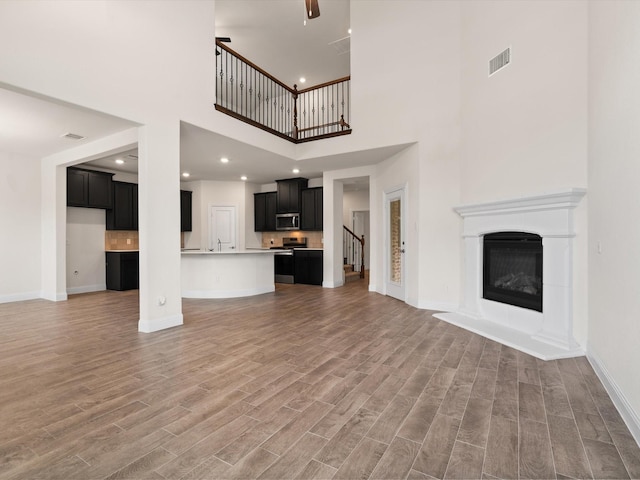 6020 Paddock Ln, Little Elm, TX 76227 - unfurnished living room with a high ceiling, baseboards, light wood finished floors, a glass covered fireplace, and stairs