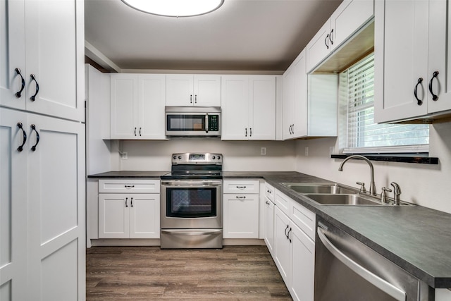 kitchen with stainless steel appliances, a sink, dark countertops, and white cabinets