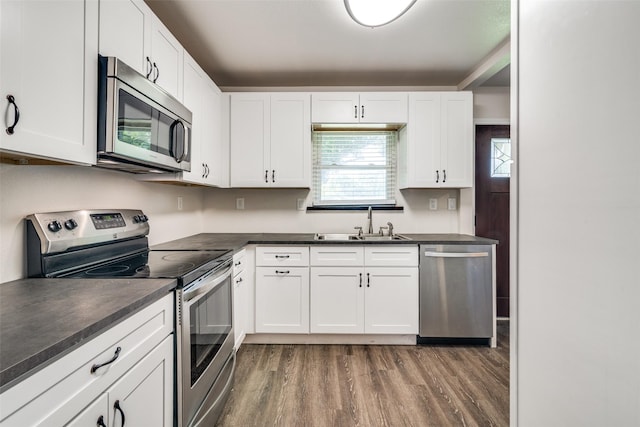 kitchen featuring appliances with stainless steel finishes, dark countertops, a sink, wood finished floors, and white cabinets