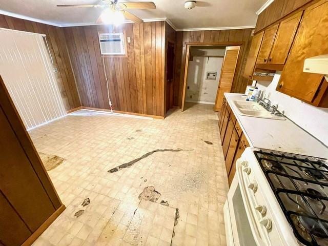 kitchen featuring ornamental molding, white gas range oven, a ceiling fan, wooden walls, and brown cabinets