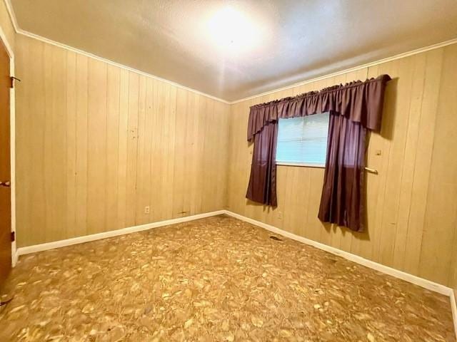 empty room with wood walls, crown molding, and baseboards
