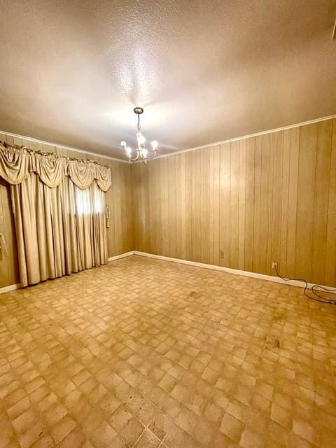 empty room featuring a chandelier, wood walls, baseboards, and a textured ceiling