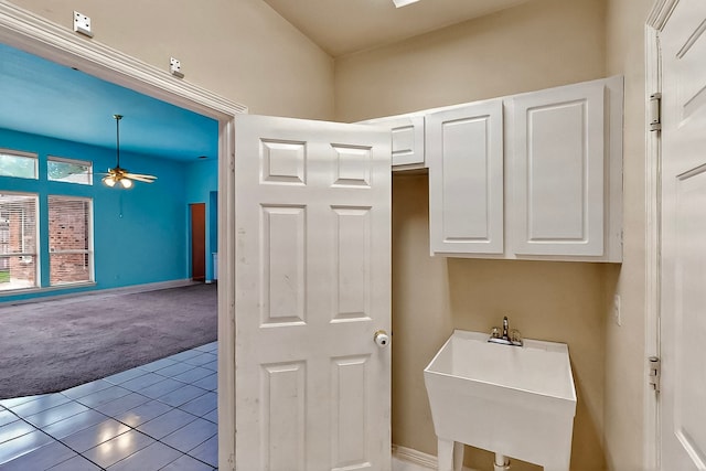 laundry area featuring carpet floors, a ceiling fan, a sink, tile patterned flooring, and baseboards