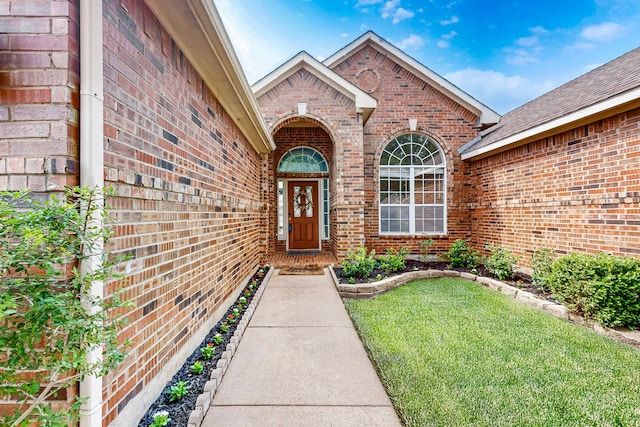 view of exterior entry with brick siding and a lawn