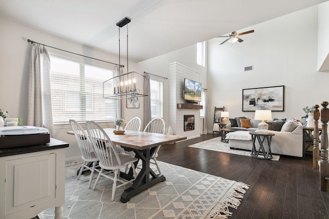 7205 Wildflower Way, Little Elm, TX 76227 - dining room with ceiling fan, a large fireplace, wood finished floors, a chandelier, and high vaulted ceiling