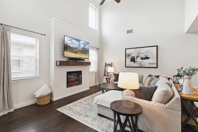 7205 Wildflower Way, Little Elm, TX 76227 - living area with a ceiling fan, a large fireplace, dark wood-style floors, healthy amount of natural light, and a towering ceiling