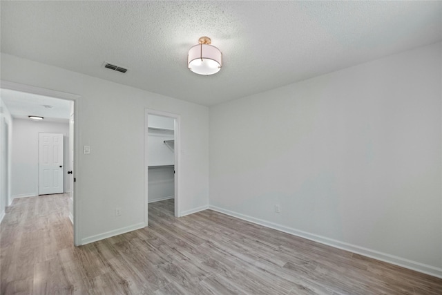 1100 Hyde Park Dr, Mckinney, TX 75069 - unfurnished bedroom featuring light wood finished floors, baseboards, a walk in closet, a closet, and a textured ceiling