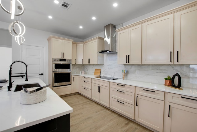 kitchen with wall chimney exhaust hood, cream cabinetry, a sink, light countertops, and backsplash