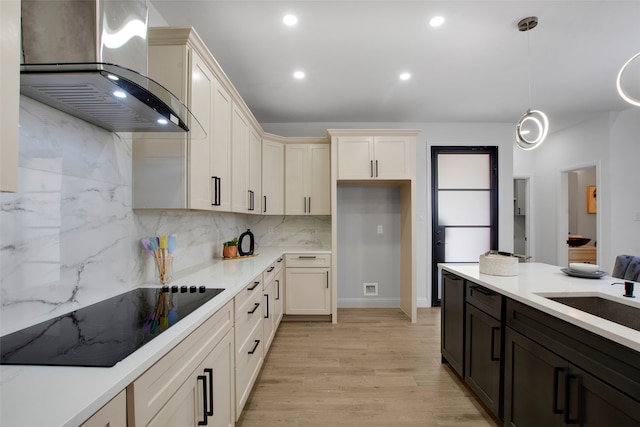 kitchen featuring wall chimney exhaust hood, black electric stovetop, light wood-style floors, a sink, and decorative light fixtures