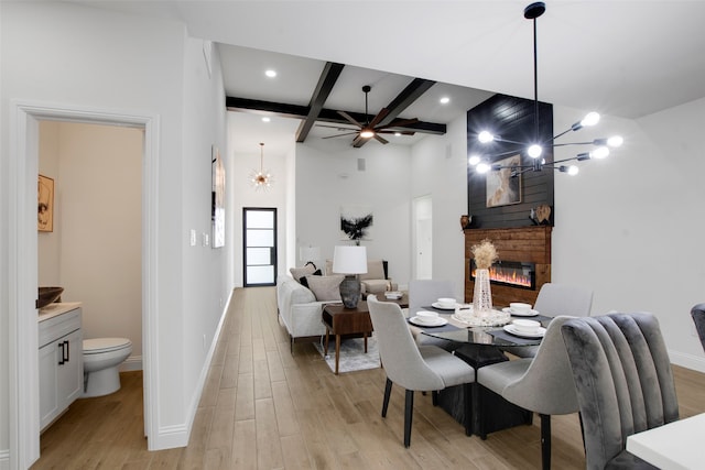 dining space featuring a glass covered fireplace, baseboards, light wood-style floors, beamed ceiling, and ceiling fan