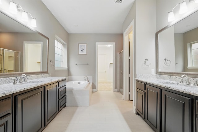 full bathroom featuring healthy amount of natural light, a bath, two vanities, and tile patterned flooring